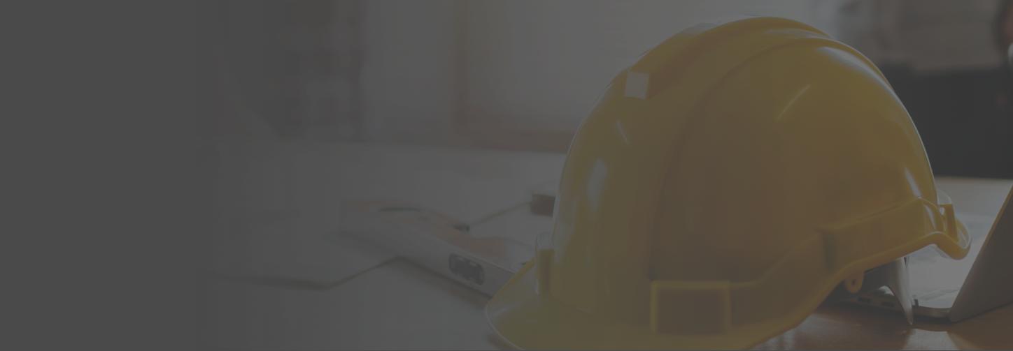 A construction hard hat in focus on top of an office desk surrounded by business documents